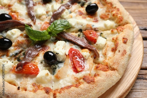 Tasty pizza with anchovies, basil and olives on wooden table, closeup