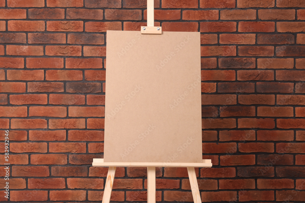 Wooden easel with blank board near brick wall - obrazy, fototapety, plakaty 