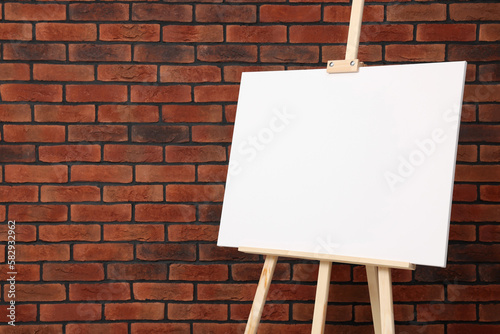 Wooden easel with blank canvas near brick wall, closeup. Space for text