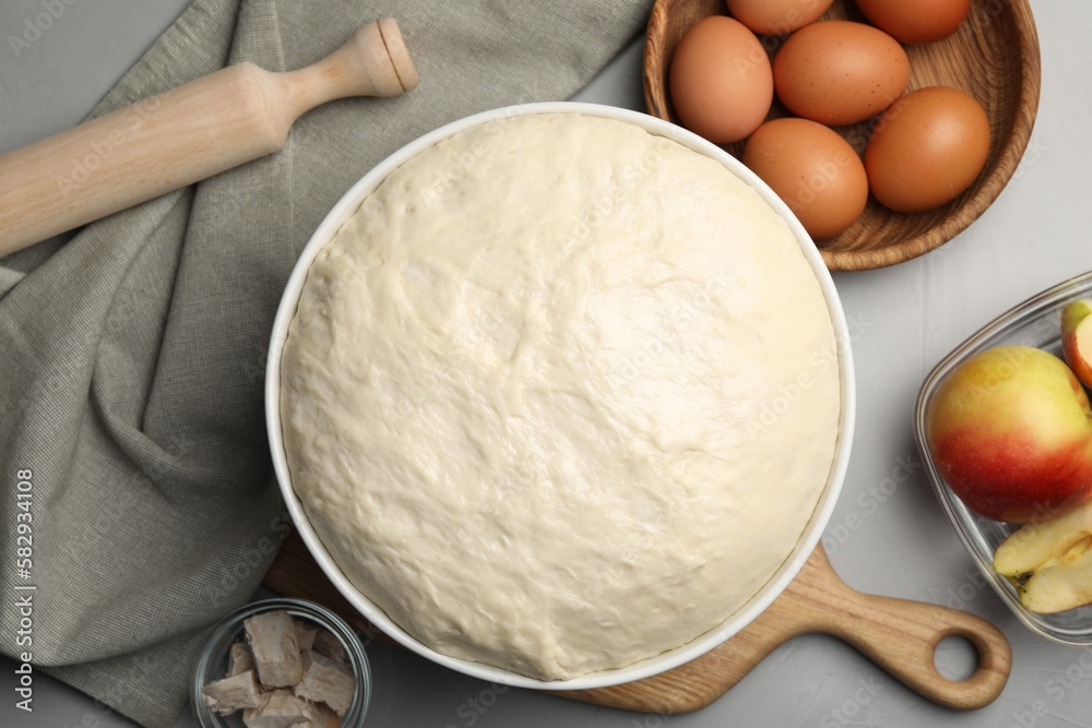 Fresh dough, rolling pin and ingredients on grey table, flat lay. Cooking yeast cake Fresh dough, rolling pin and ingredients on grey table, flat lay. Cooking yeast cake