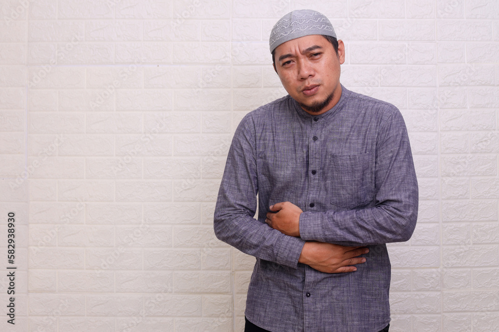 Asian muslim man squeeze his stomach feeling hungry during fasting on ramadan isolated over white background Asian muslim man squeeze his stomach feeling hungry during fasting on ramadan isolated over white background