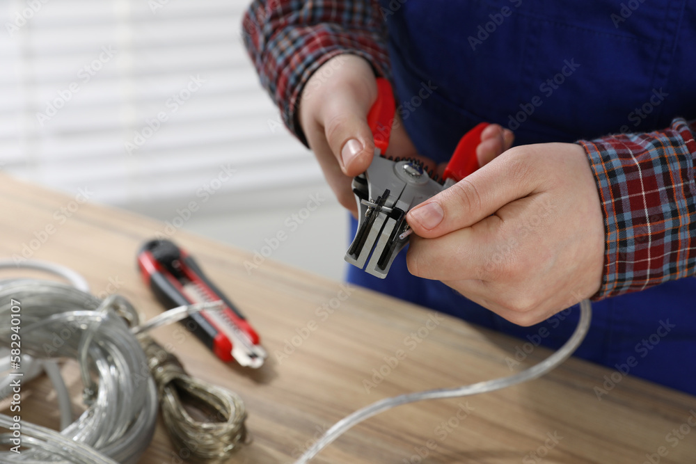 Fototapeta premium Professional electrician stripping wiring at wooden table, closeup view