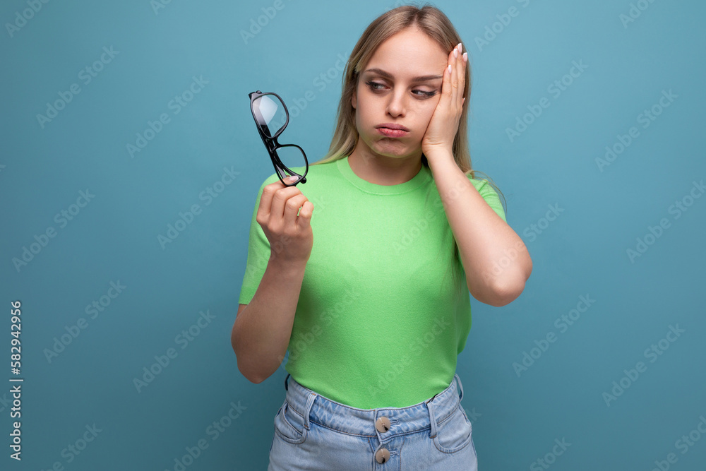 upset woman holding eyeglasses and holding her head on blue background upset woman holding eyeglasses and holding her head on blue background