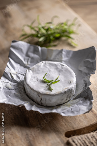 Opened package of brie cheese with a spring of rosemary on top with a rustick background