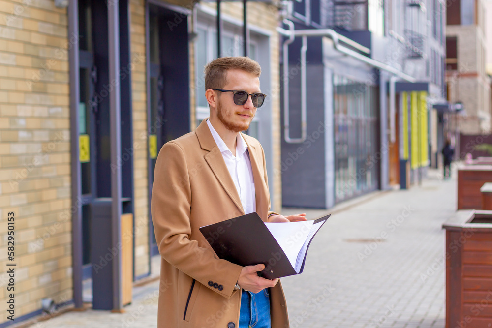 Portrait of a handsome man, businessman, scientist or teacher. He walks along a modern city street with a folder of documents and a notebook in his hands Portrait of a handsome man, businessman, scientist or teacher. He walks along a modern city street with a folder of documents and a notebook in his hands