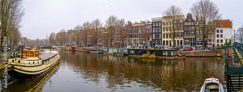 Amsterdam downtown panoramic skyline, boat canal, traditional houses, bridges, and walkway on an overcast morning with the serene reflection of lights in the water, in the Netherlands