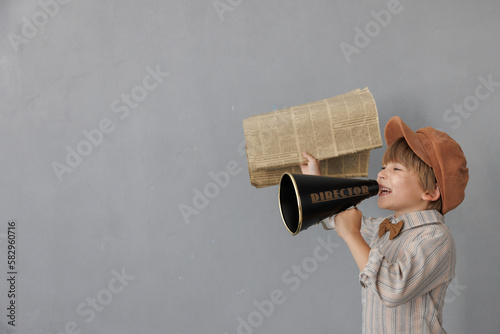 Newsboy shouting against grunge wall background. Boy selling newspaper photo