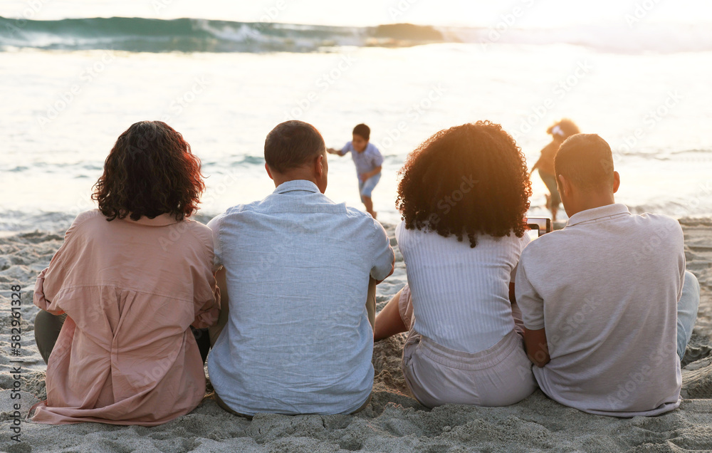 Family sitting on beach from the back, sunset and view of waves, zen and children playing in water together. Holiday, men and women relax in peace at evening ocean in Indonesia on tropical vacation. Family sitting on beach from the back, sunset and view of waves, zen and children playing in water together. Holiday, men and women relax in peace at evening ocean in Indonesia on tropical vacation.