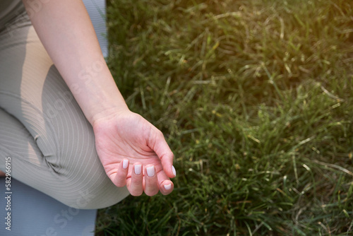 Close-up of a woman's hands on a background of green grass and a gymnastic mat. Young woman practices yoga in the park.