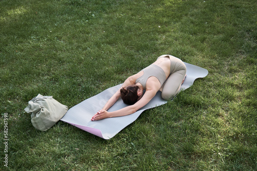 A young positive woman in a gymnastic suit practices yoga and meditates while sitting on a mat.