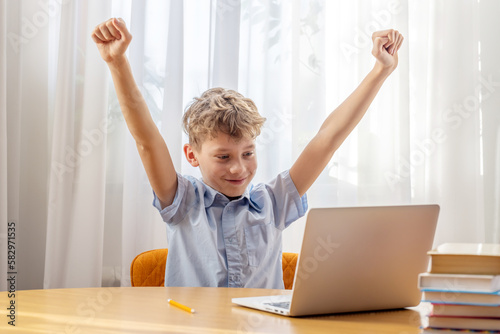 Excited schoolboy learning online on laptop