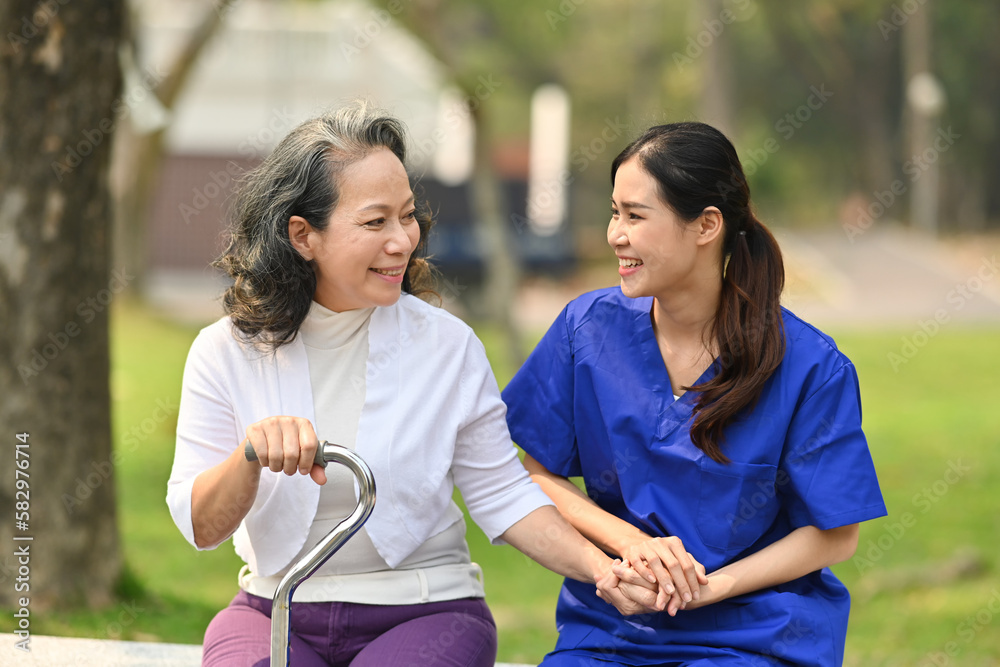 Positive female nurse in uniform having pleasant conversation with senior woman in the garden at home care Positive female nurse in uniform having pleasant conversation with senior woman in the garden at home care