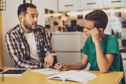 Father is helping his son with learning. They are doing homework together.