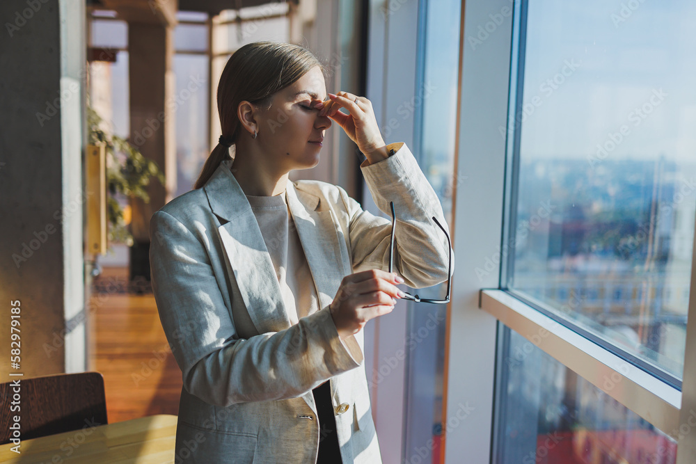 Headache in young business woman in casual clothes and glasses in office. Migraine from office work.