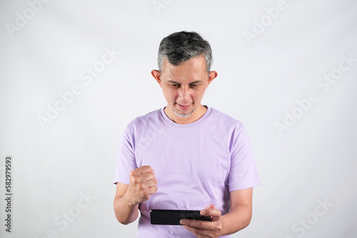 Portrait of a satisfied Asian man with casual purple tshirt celebrating success isolated over white background.
