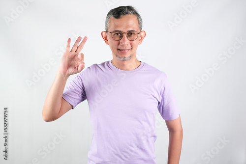 Asian handsome grey-haired man wearing purple tshirt over isolated white background smiling positive doing ok sign with hand and fingers. Successful expression. 