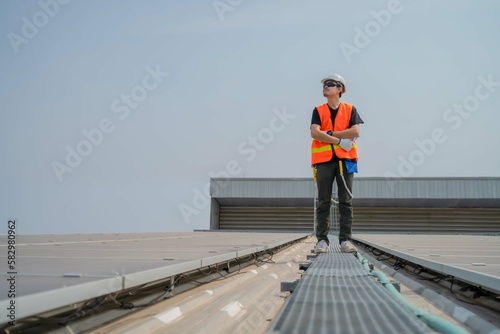 Asian engineers wearing protective vest and white hardhat standing on roof crossed arms and looking to the copy space while holding tablet.