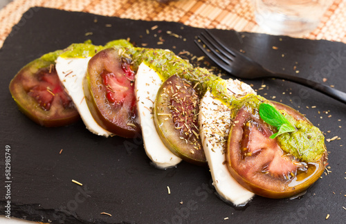 caprese salad with mozzarella, black tomatoes and pesto on black stone plate photo