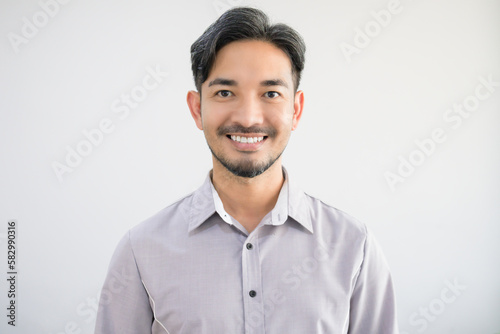 Portrait of a handsome Asian man with a beard in a gray shirt making a smile face.