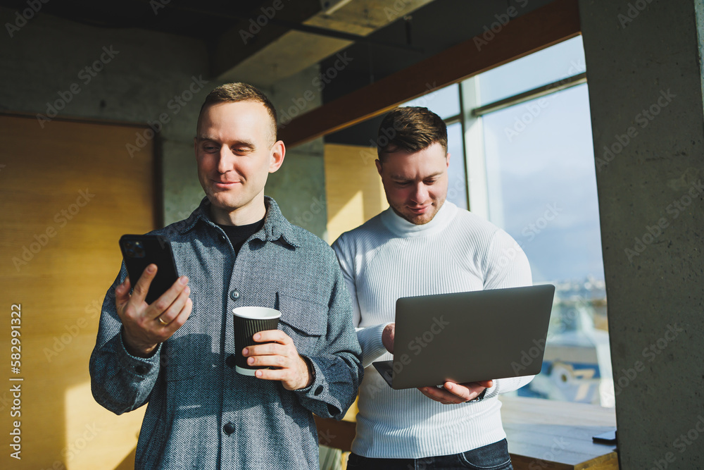 Work of two male colleagues standing in office together while