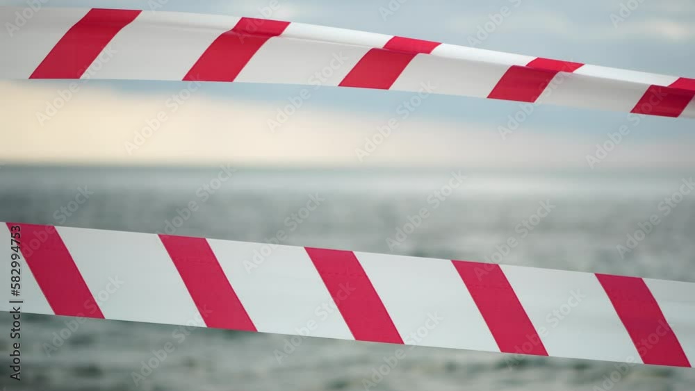 Red white warning tape barrier ribbon swinging in the wind across exotic sea beach background without people. No entry Red White caution tape. No holiday concept, delayed travel, no summer plans Red white warning tape barrier ribbon swinging in the wind across exotic sea beach background without people. No entry Red White caution tape. No holiday concept, delayed travel, no summer plans