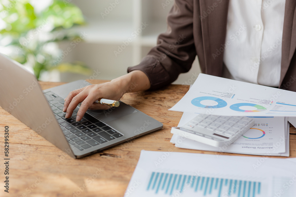 Close-up shot of businesswoman using calculator and laptop to calculate company financial result On wooden table in office and business background, tax, accounting, statistics and analytical research. Close-up shot of businesswoman using calculator and laptop to calculate company financial result On wooden table in office and business background, tax, accounting, statistics and analytical research.