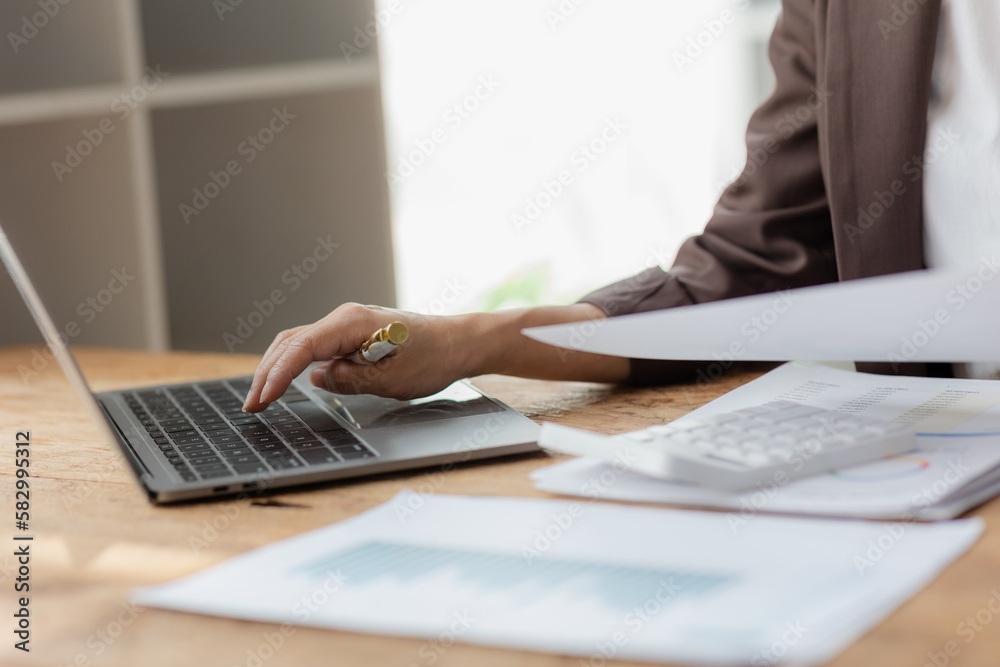 Close-up shot of businesswoman using calculator and laptop to calculate company financial result On wooden table in office and business background, tax, accounting, statistics and analytical research. - obrazy, fototapety, plakaty 