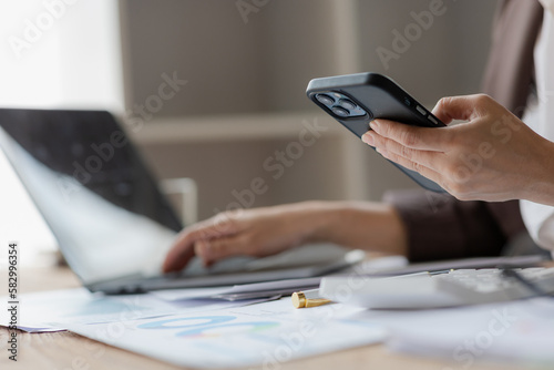 Close-up shot of asian businesswoman using laptop and smart phone for doing financial mathematics on wooden table, tax, accounting, statistics and analytical research concept.
