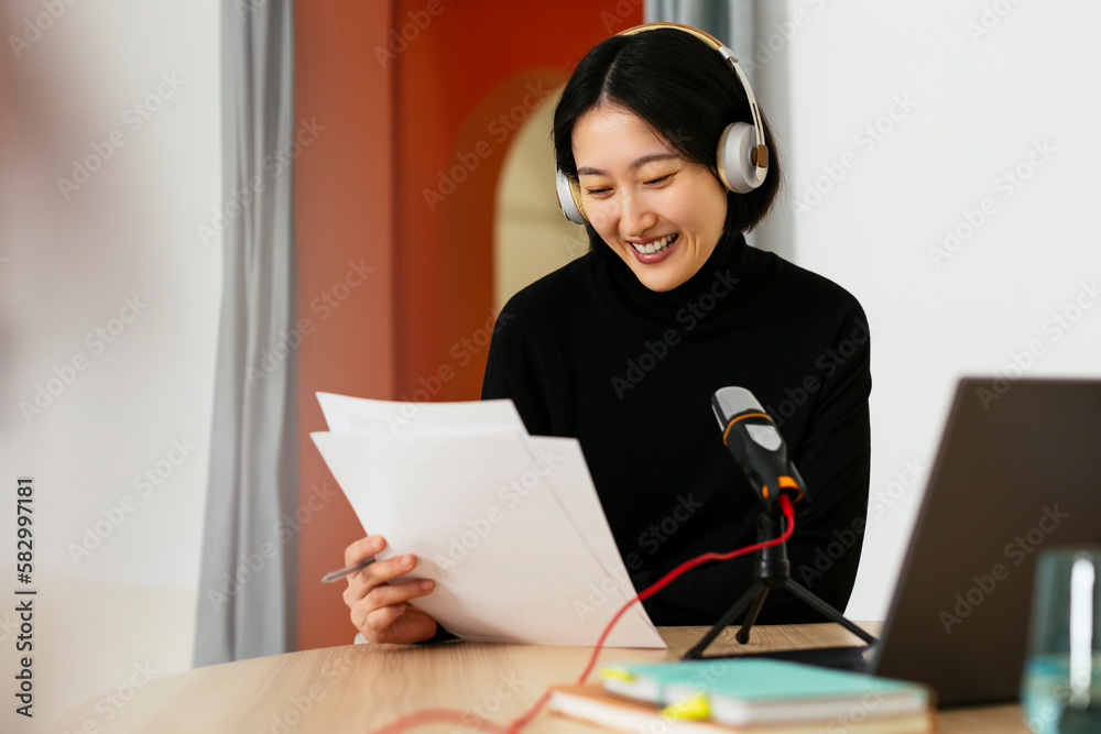 Happy woman wearing headphones reading documents in podcast studio Happy woman wearing headphones reading documents in podcast studio