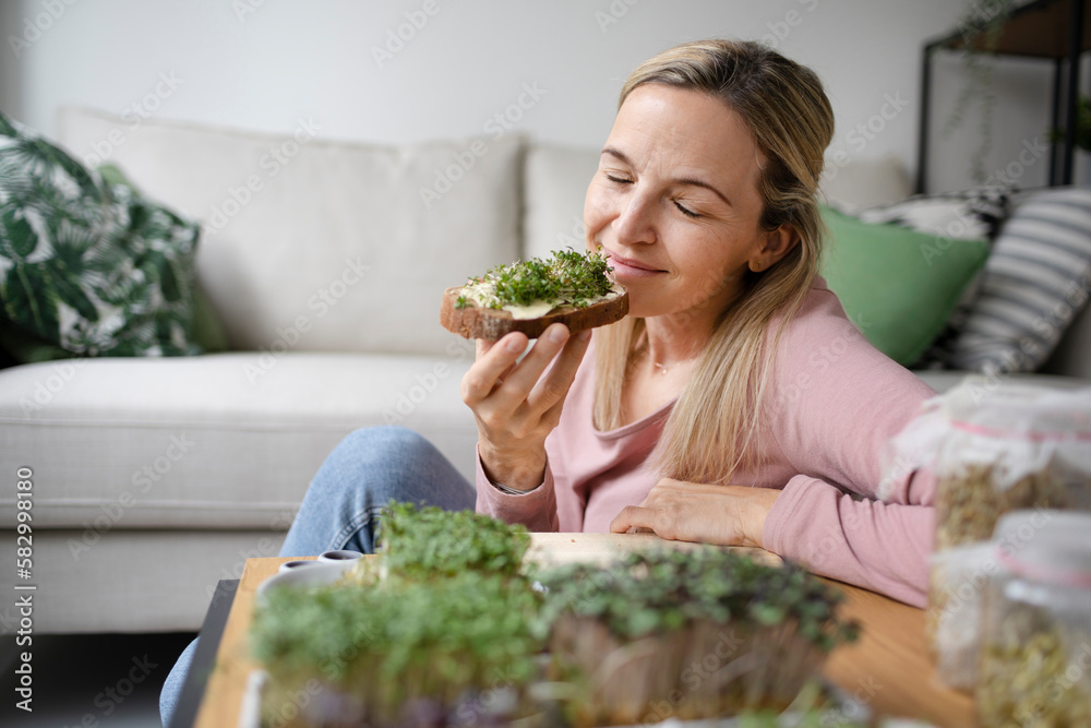 Smiling woman with eyes closed enjoying sprouts on bread at home Smiling woman with eyes closed enjoying sprouts on bread at home