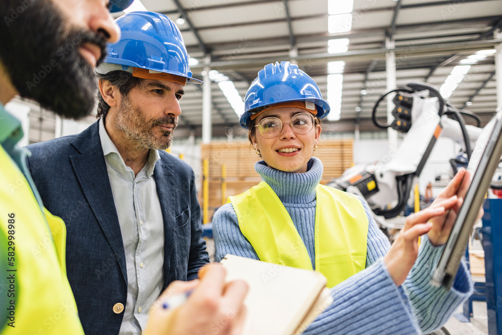 Smiling engineer discussing over tablet PC with colleagues in factory Smiling engineer discussing over tablet PC with colleagues in factory