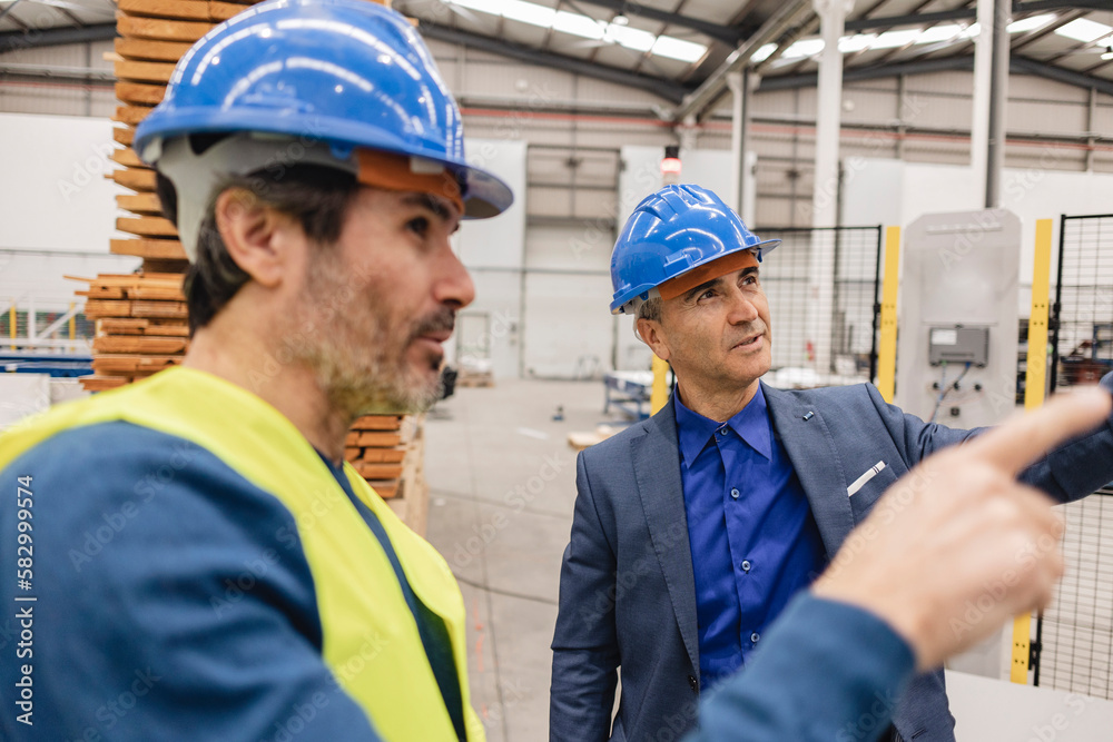 Mature engineers wearing hardhat having discussions in robotics factory