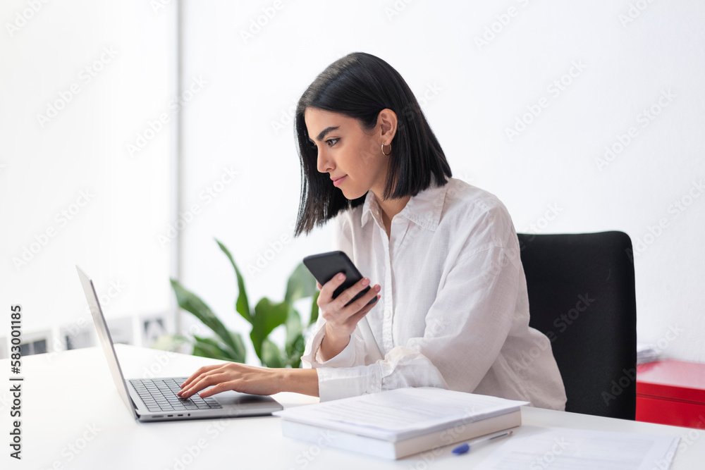 Young businesswoman with smart phone using laptop at desk Young businesswoman with smart phone using laptop at desk
