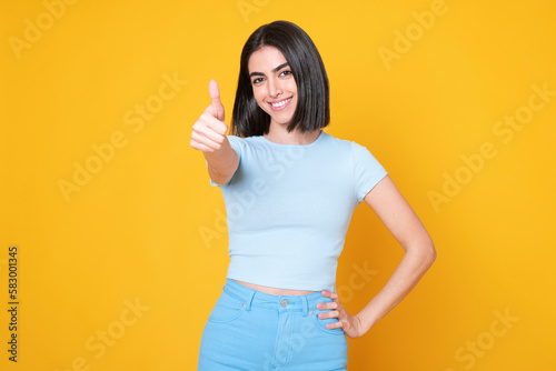 Happy woman showing thumbs up gesture against yellow background