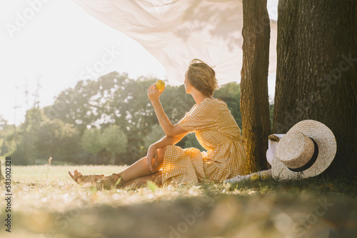 Woman sitting with fruit by tree trunk at park photo