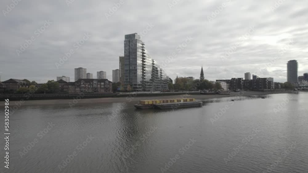 Highrise modern apartment house with glossy glass facade. Fly over loaded cargo ships standing on river. London, UK Highrise modern apartment house with glossy glass facade. Fly over loaded cargo ships standing on river. London, UK