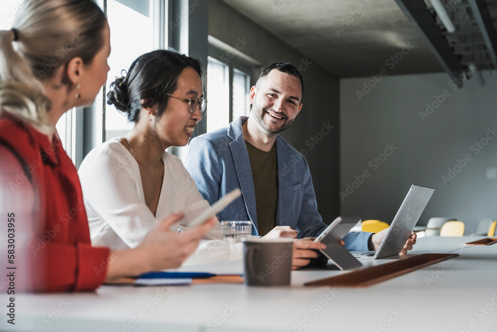 Smiling businessman with laptop sitting with colleagues at office Smiling businessman with laptop sitting with colleagues at office