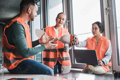Multiracial colleagues wearing reflective clothing testing wind turbine rotor in meeting at office