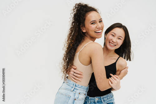 Two cheerful girls hugging while posing isolated over white wall