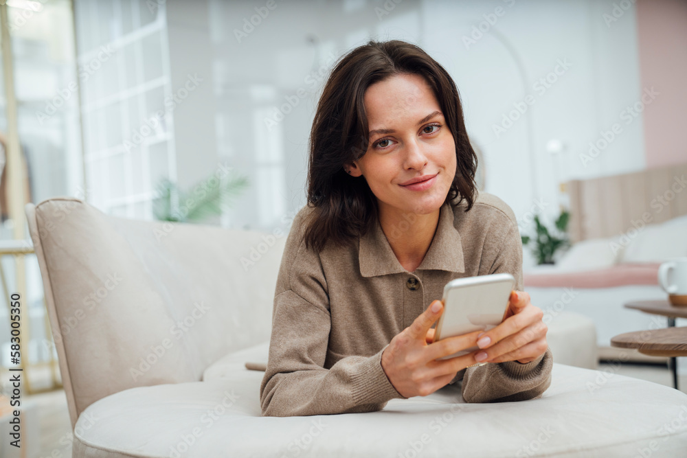 Smiling young woman with mobile phone lying on sofa at home Smiling young woman with mobile phone lying on sofa at home