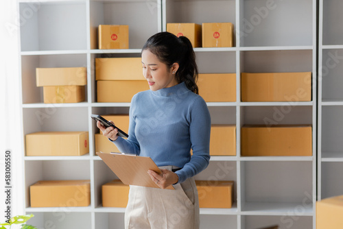 Startup  small business  SME  Asian female entrepreneur owner uses smartphones to talk to customers online and check online orders to prepare packages. Sell Ideas Online.