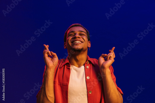 Smiling african man holding fingers crossed for good luck isolated