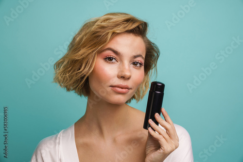 Young woman showing cosmetic bottle isolated over blue background