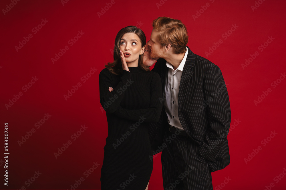 Surprised young couple gossiping isolated over red wall Surprised young couple gossiping isolated over red wall