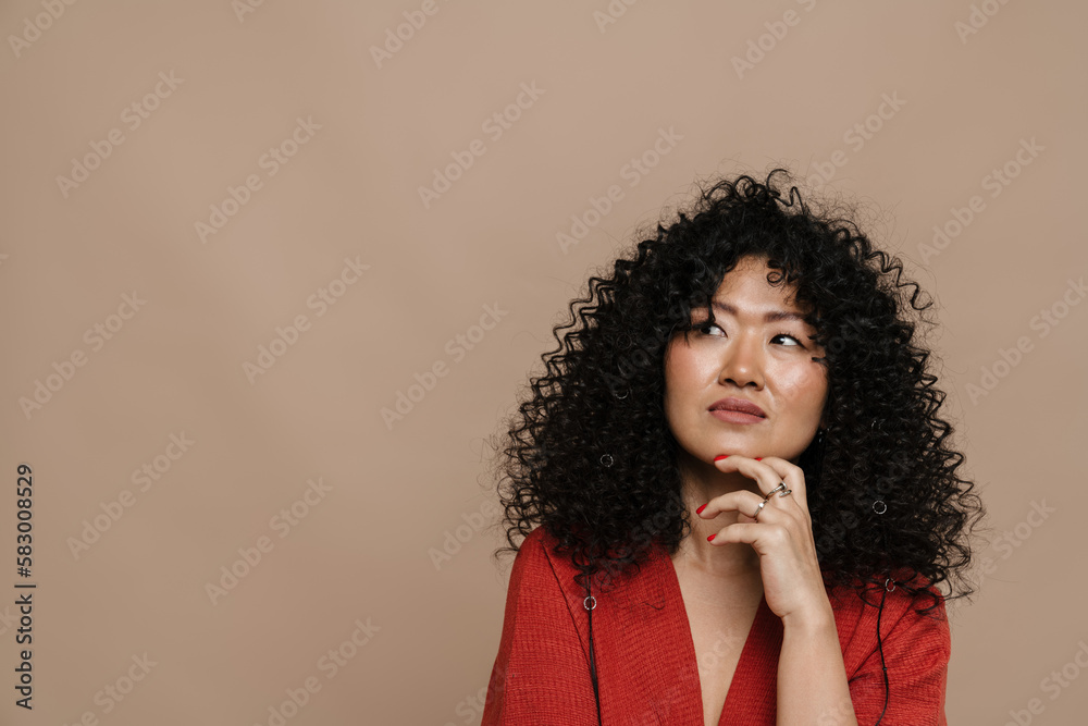 Thoughtful asian woman touching her chin and looking away while standing isolated Thoughtful asian woman touching her chin and looking away while standing isolated