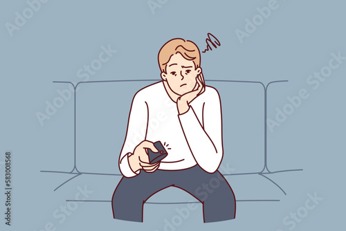 Bored man holding TV remote due to lack of satellite TV channels with interesting shows. Concept frustration and procrastination associated with lack of motivation caused by emotional burnout 