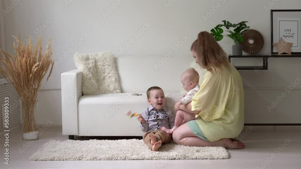 A mother or a nanny sits on the floor in a bright room with a baby in her arms, the older boy shows jealousy. High-quality shooting in 4k format A mother or a nanny sits on the floor in a bright room with a baby in her arms, the older boy shows jealousy. High-quality shooting in 4k format