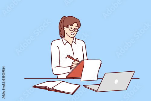 Successful businesswoman or freelancer girl working via Internet is at workplace with laptop. Woman making notes in clipboard standing near desk with laptop planning own working day 