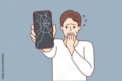 Man reacts emotionally to broken phone by bringing hand to mouth and experiencing shock due to breakdown. Guy with broken smartphone needs to replace display matrix by service center employees 