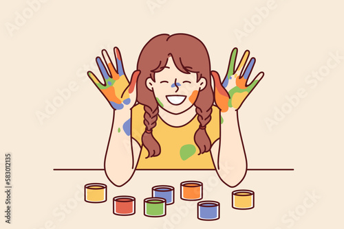 Positive girl with face and palms smeared with multi-colored paint smiles, wanting to become artist or designer. Smiling girl with gouache or watercolor on hands rejoices at school art lesson 